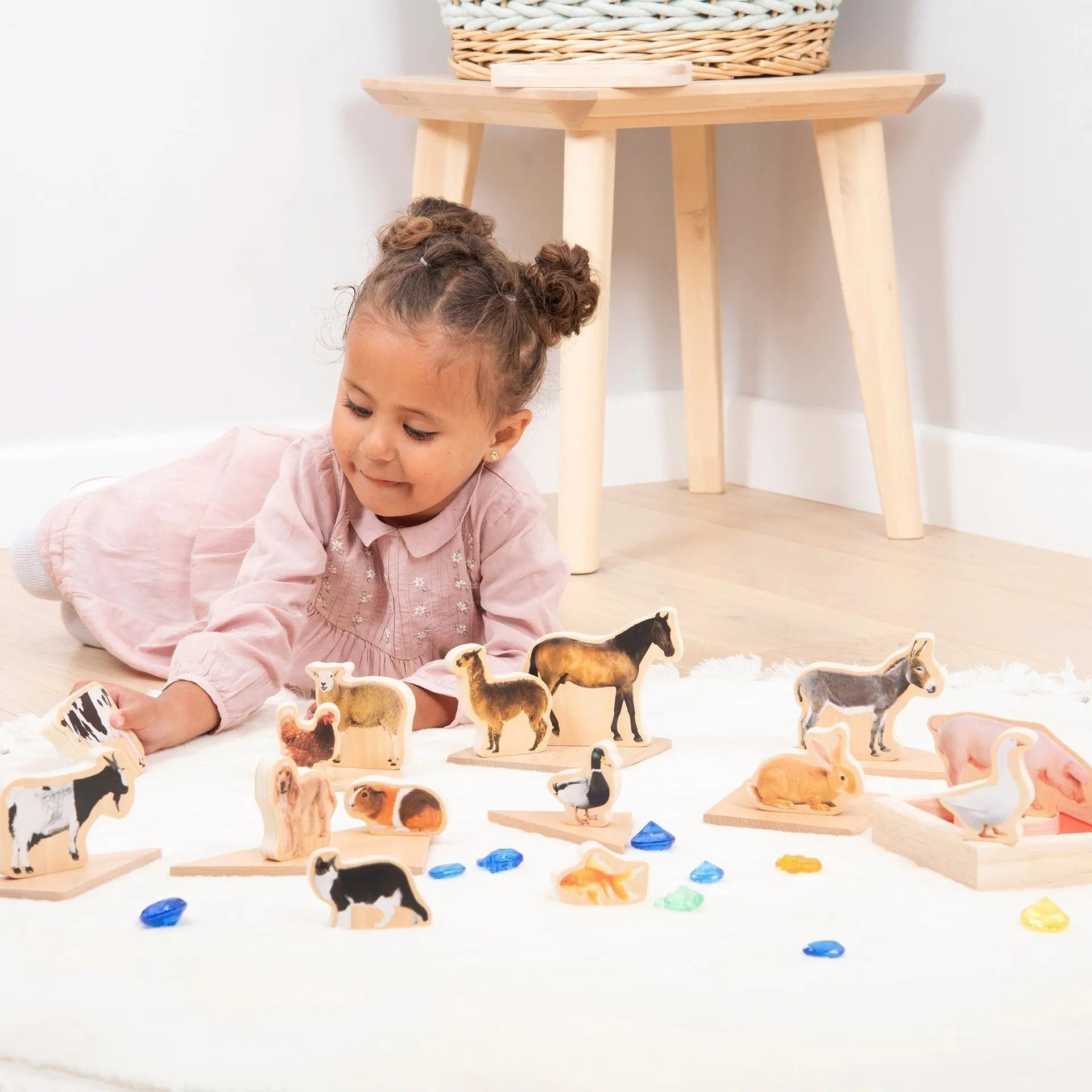 Child playing with wooden animal toys on a light-coloured floor.