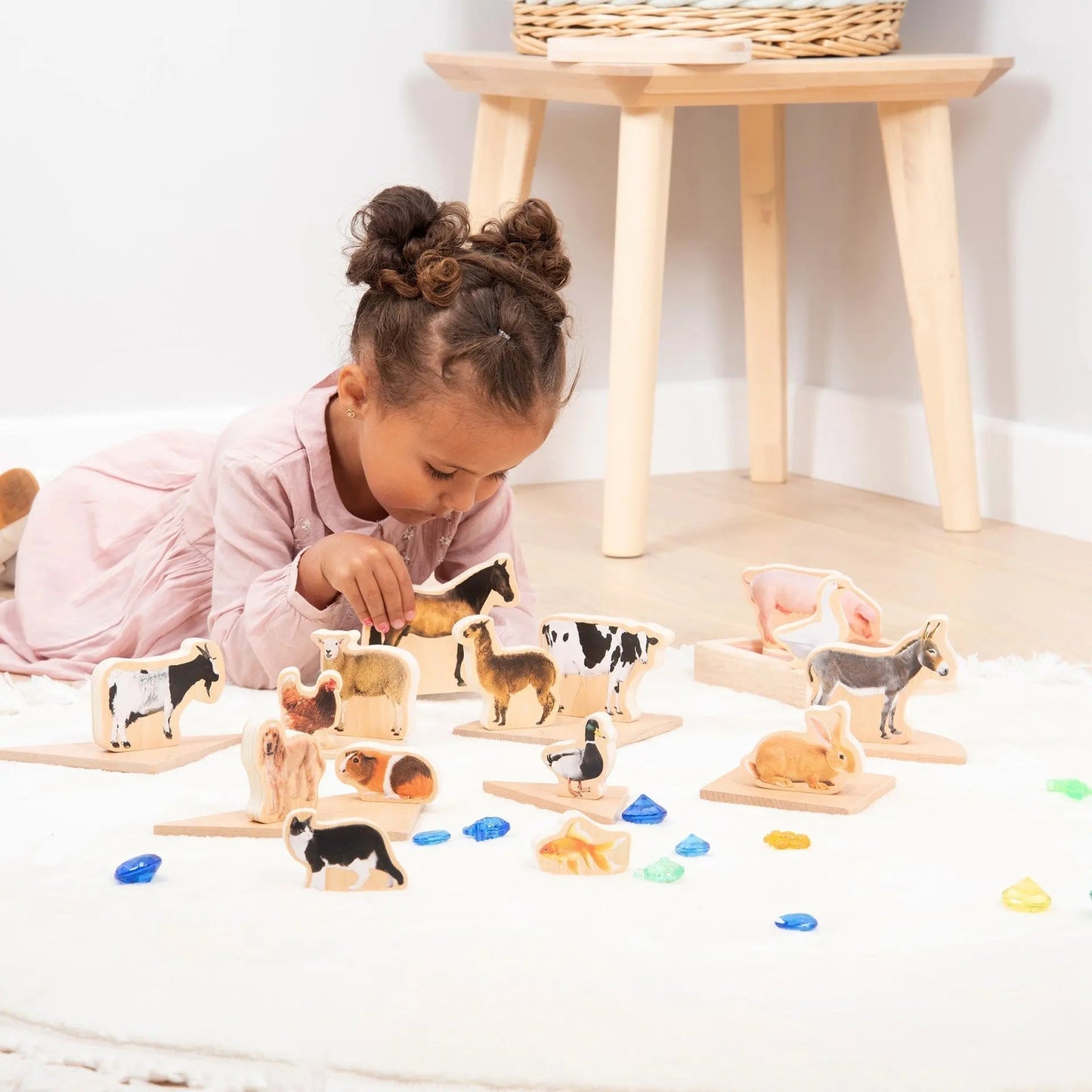 Child playing with wooden animal toys on a light-coloured floor.