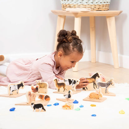 Child playing with wooden farm animal toys on a light-coloured floor.