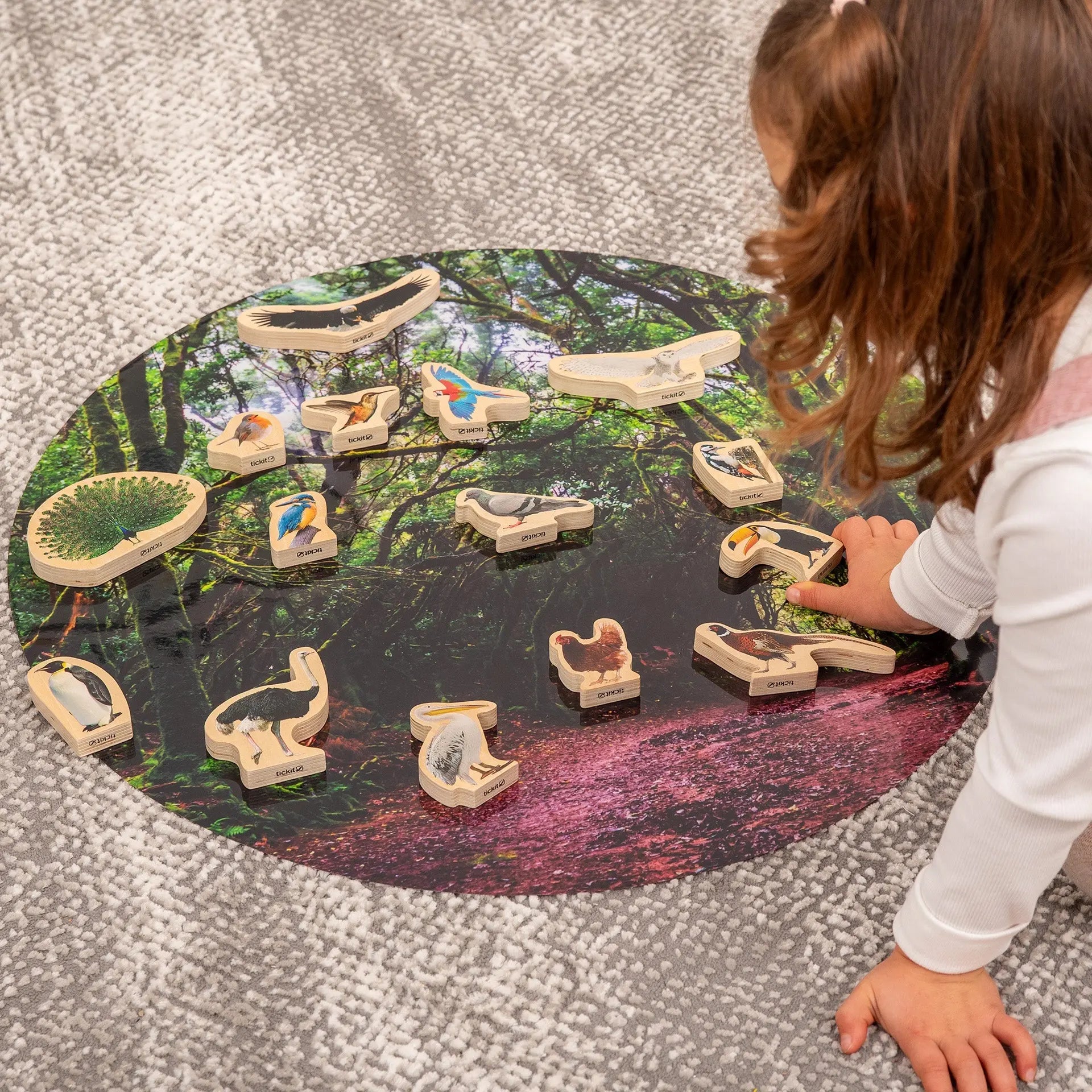 Child playing with a nature-themed wooden puzzle on a round table.