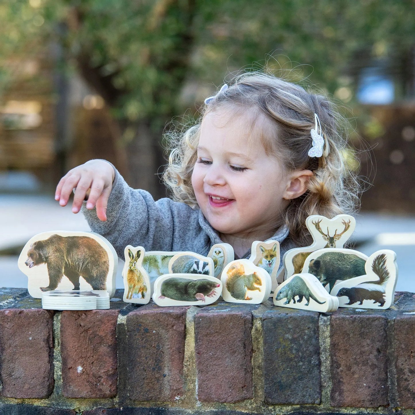 Child playing with animal figurines on a brick ledge outdoors