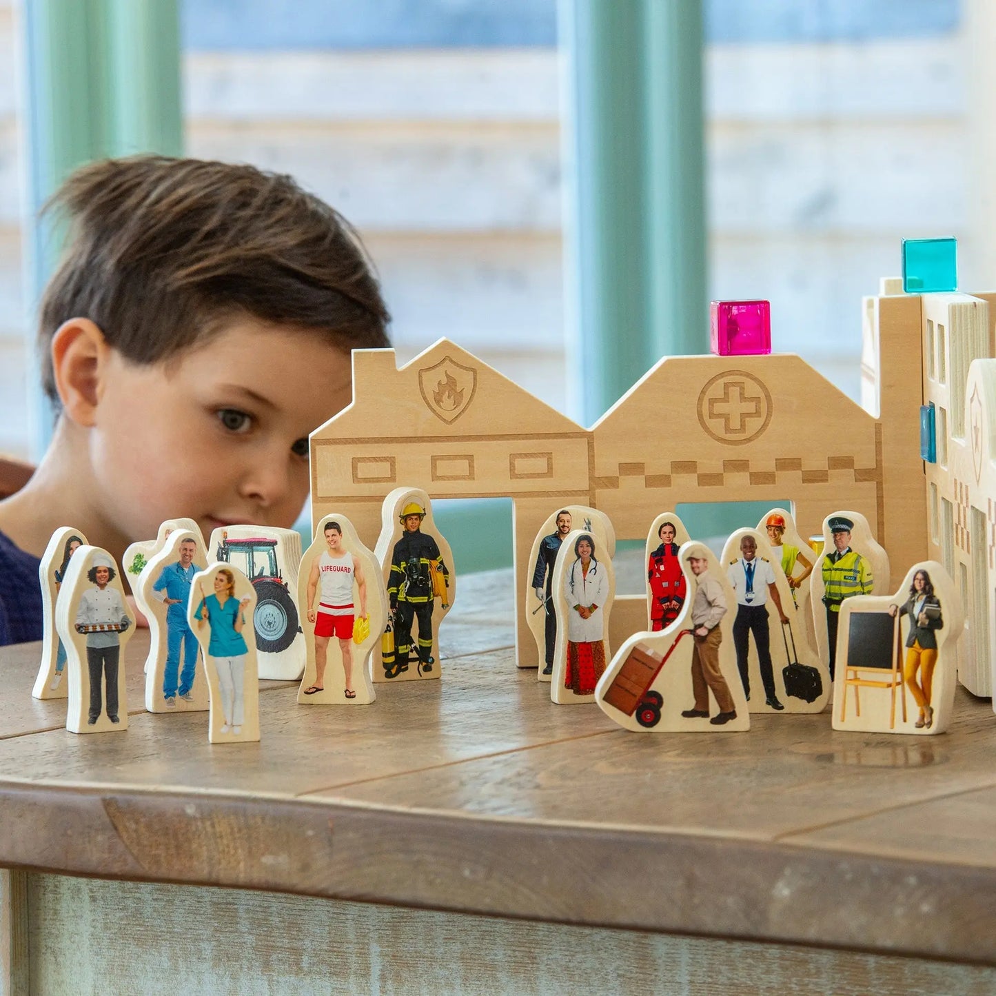 Child playing with wooden figurines and a model of a hospital, on a table.