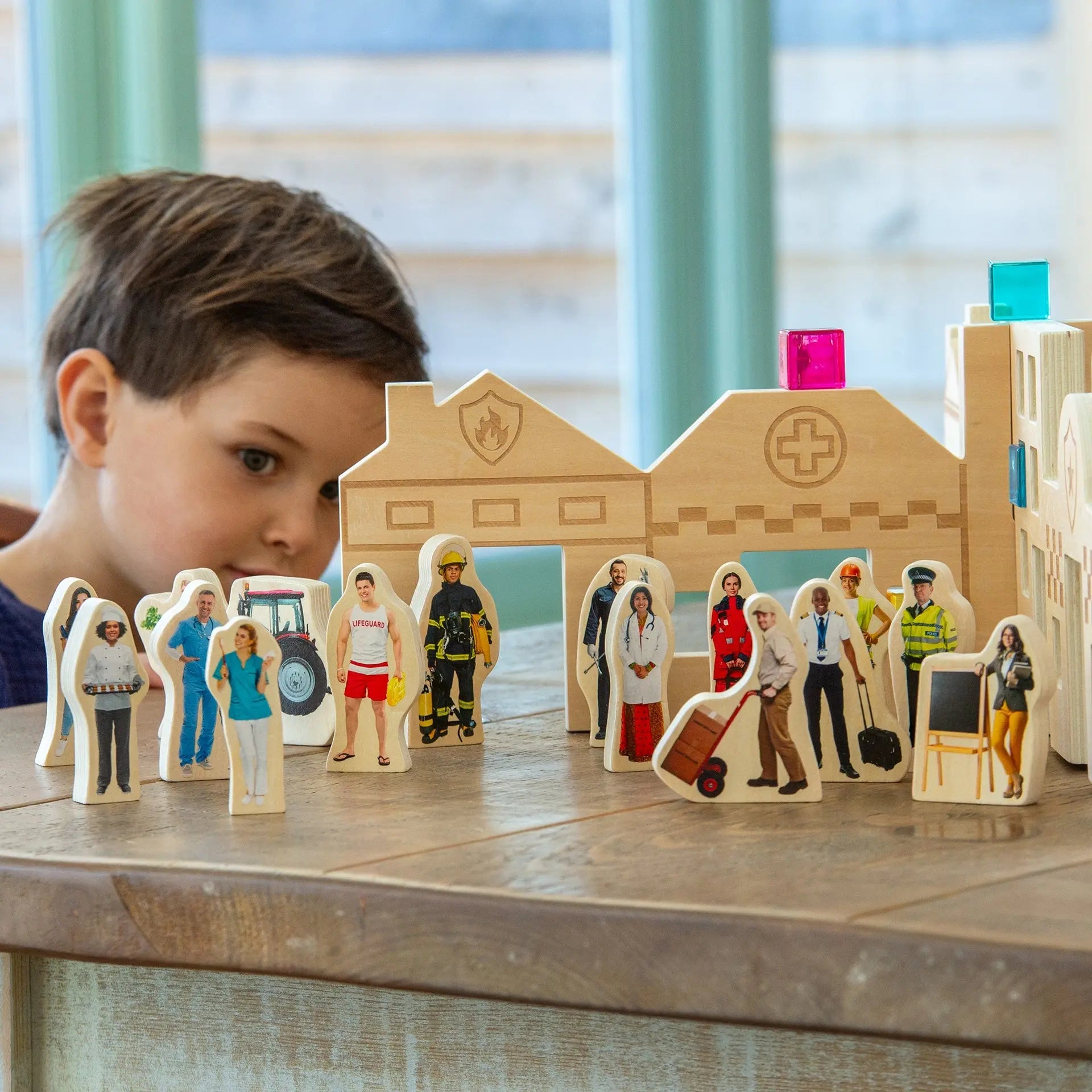 Child playing with wooden figurines and a model of a hospital, on a table.