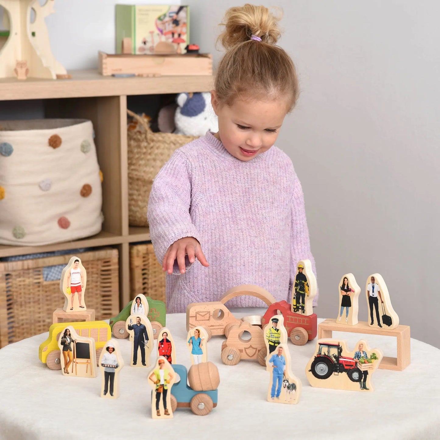 Child playing with wooden toy figures and vehicles on a table.