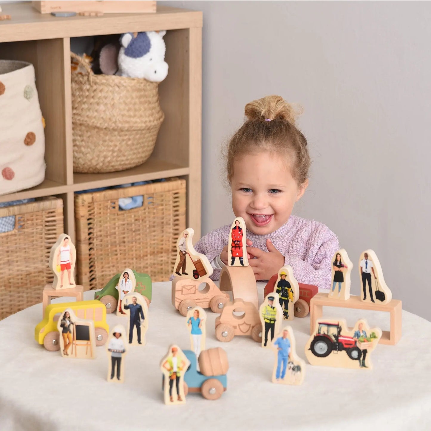 Child playing with wooden toy figures and vehicles on a table.
