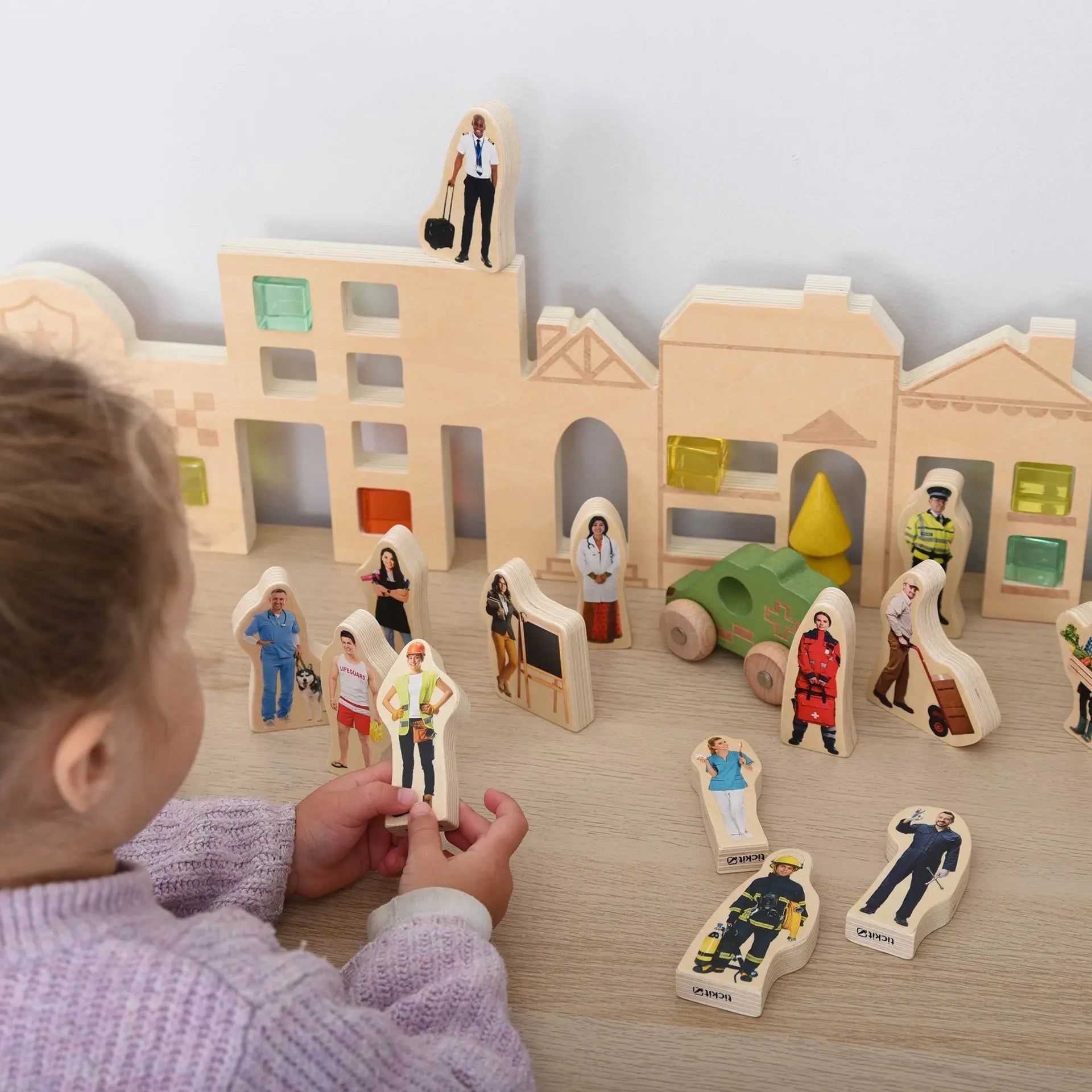 Child playing with wooden toy figures and buildings on a table