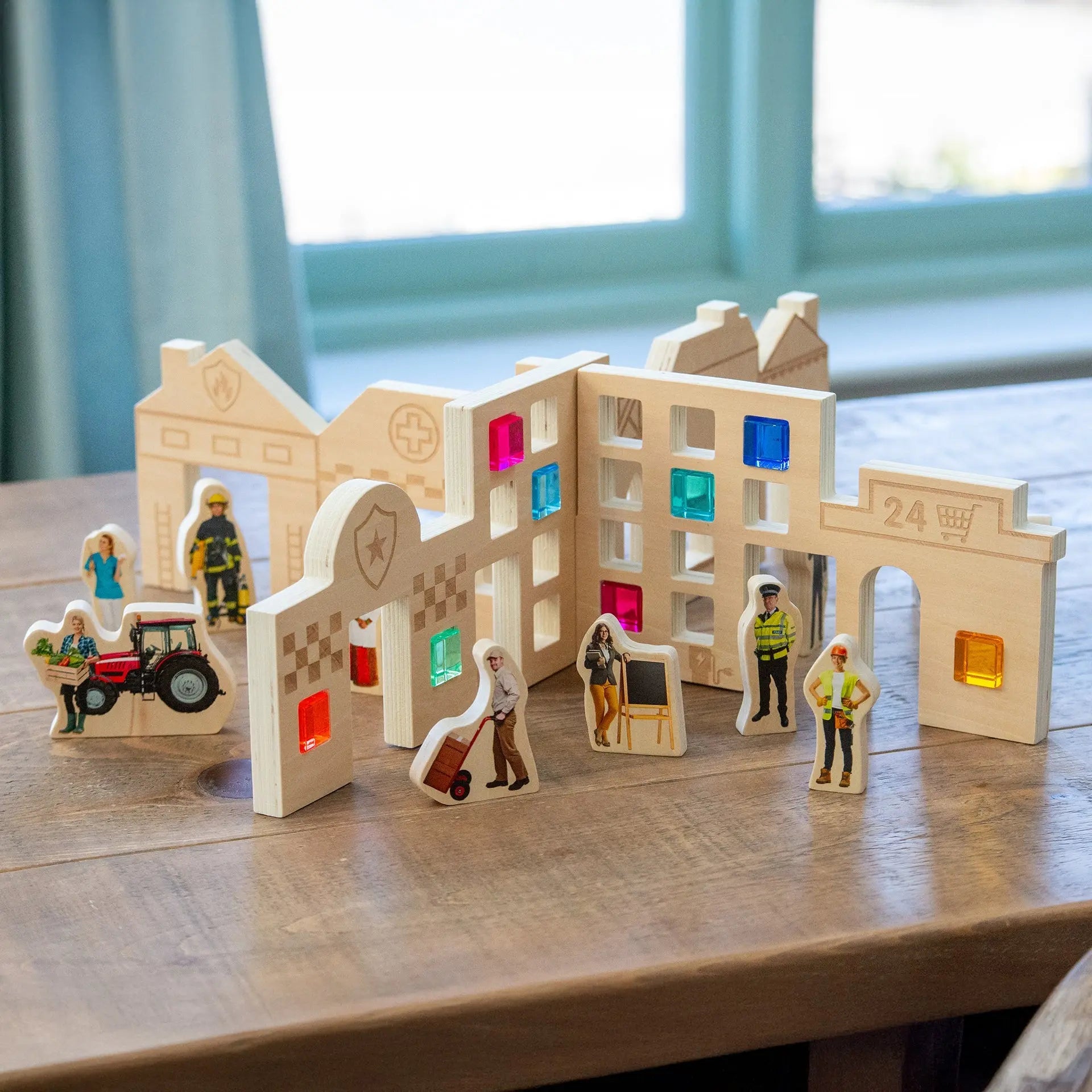 Wooden toy town set with colourful windows and small figures on a wooden surface.
