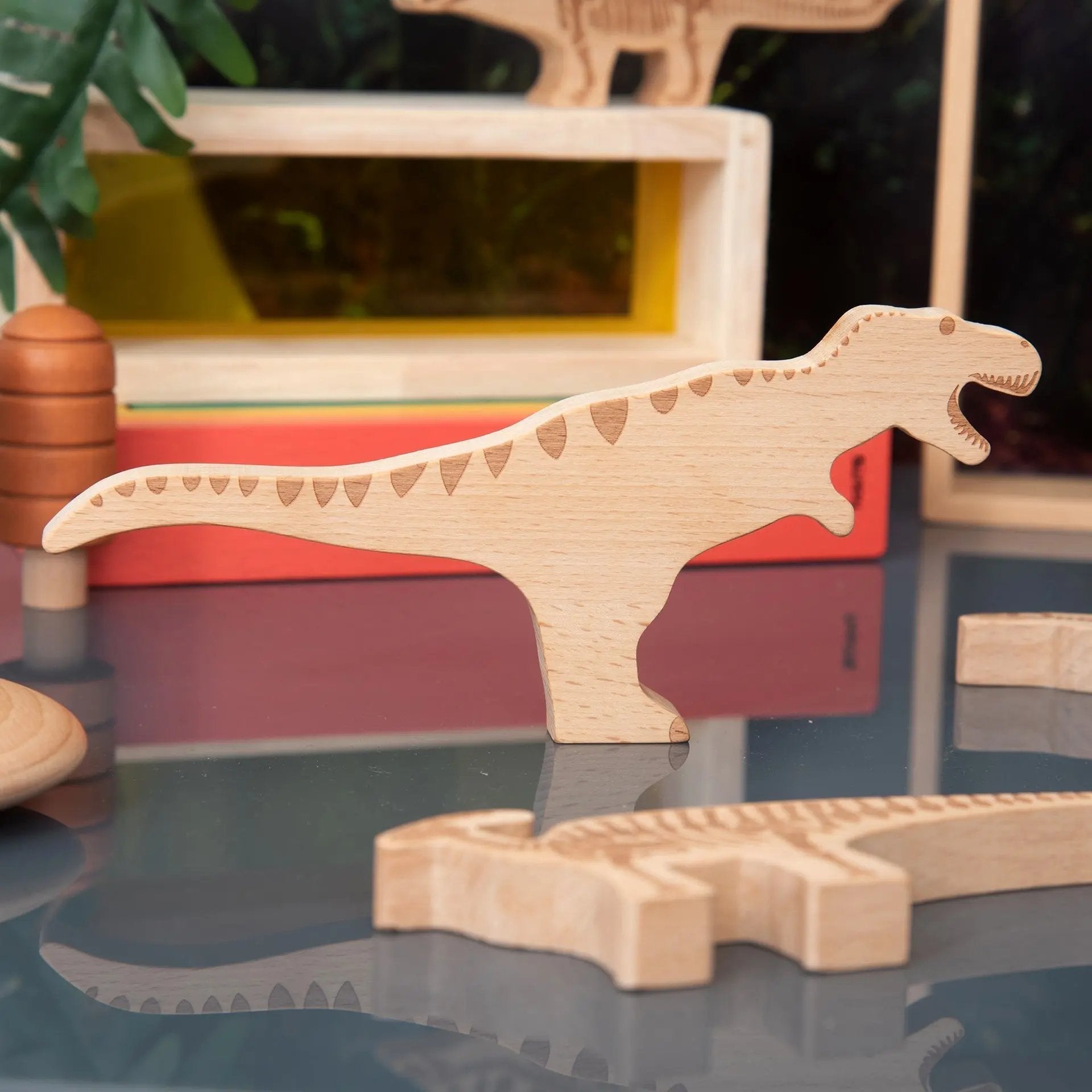 Wooden dinosaur toys on a reflective surface with a blurred background