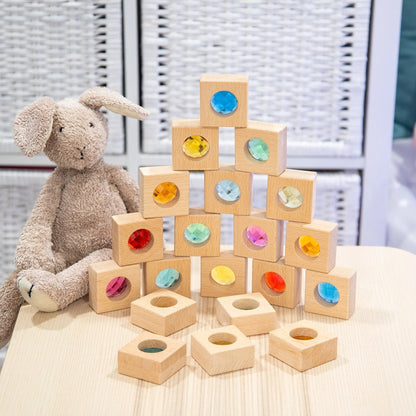 Stack of wooden blocks with colourful recessed shapes next to a plush toy on a light surface.