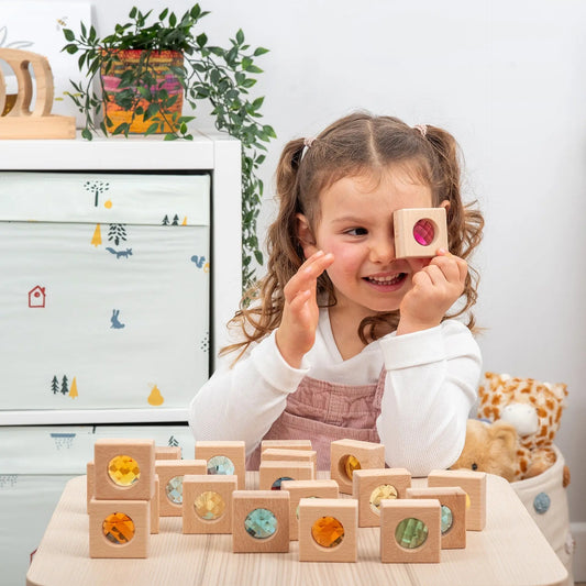 Child playing with wooden blocks in a room with a white dresser and plants.