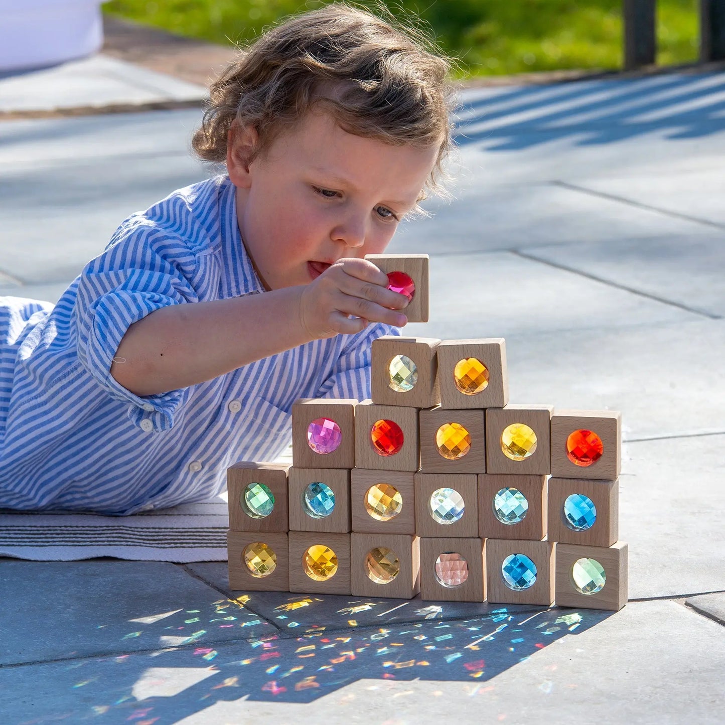 Child playing with colourful gemstone blocks on a wooden deck