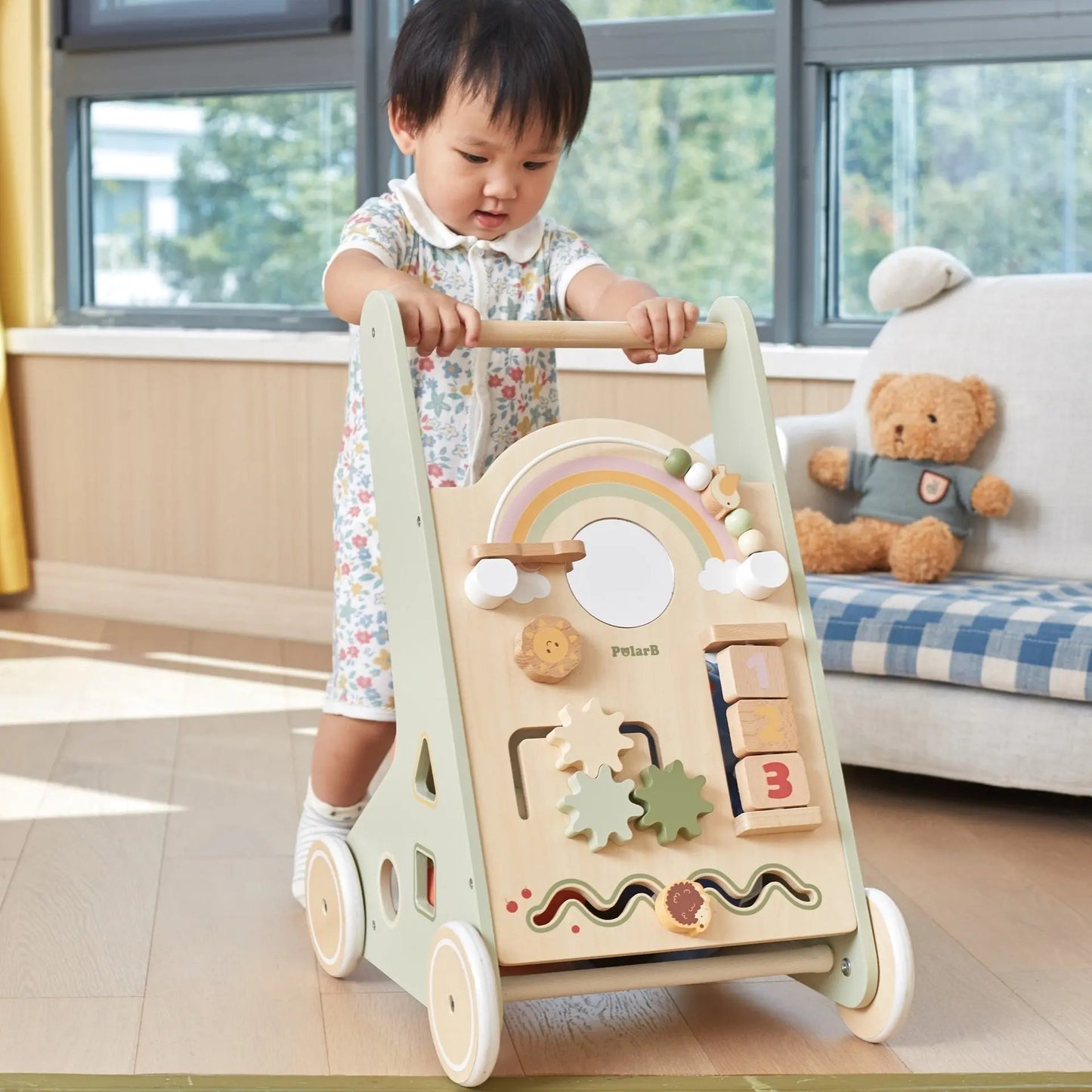 Child playing with a wooden activity walker in a room with a couch and teddy bear.