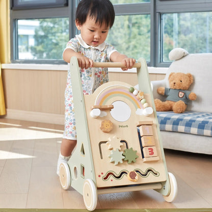 Child playing with a wooden activity walker in a room with a couch and teddy bear.