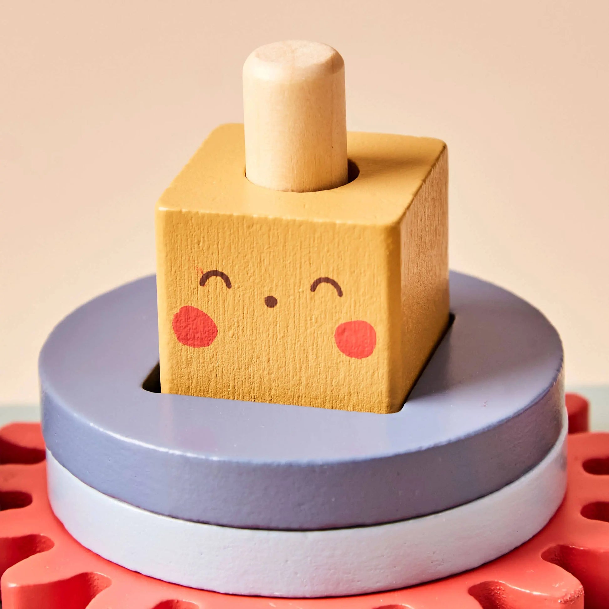 Wooden toy with a smiley face block on top of stacked rings against a beige background