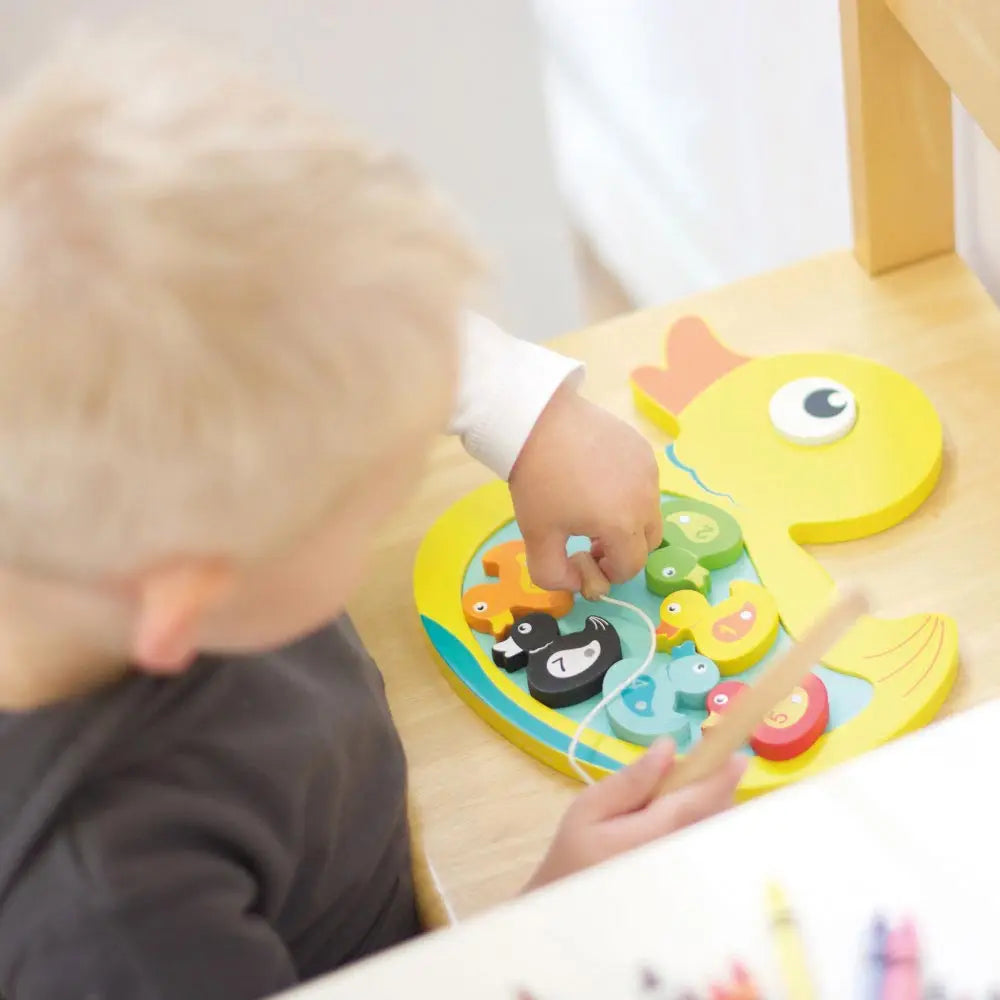 Child playing with a colourful wooden hook a duck game.