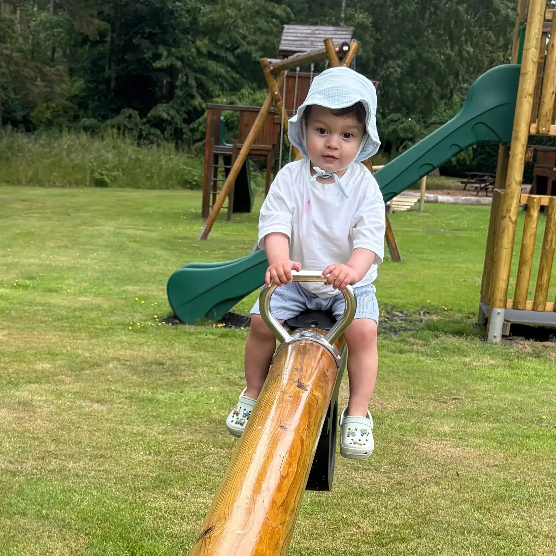 Child playing on a seesaw in a park with playground equipment in the background