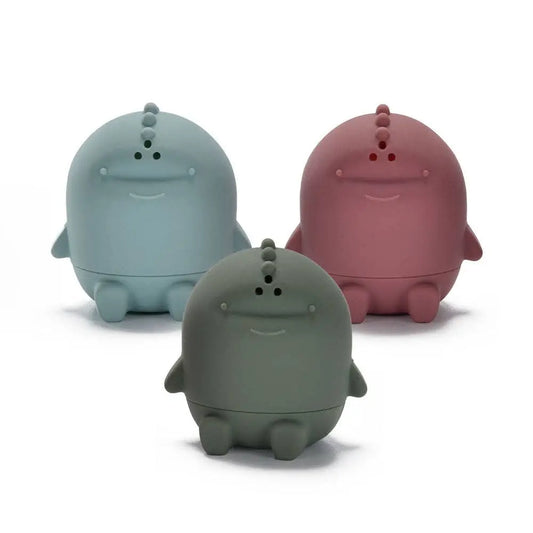 Three cute, round, dinosaur-like figurines in light blue, dusty pink, and dark grey, arranged on a clean white background.