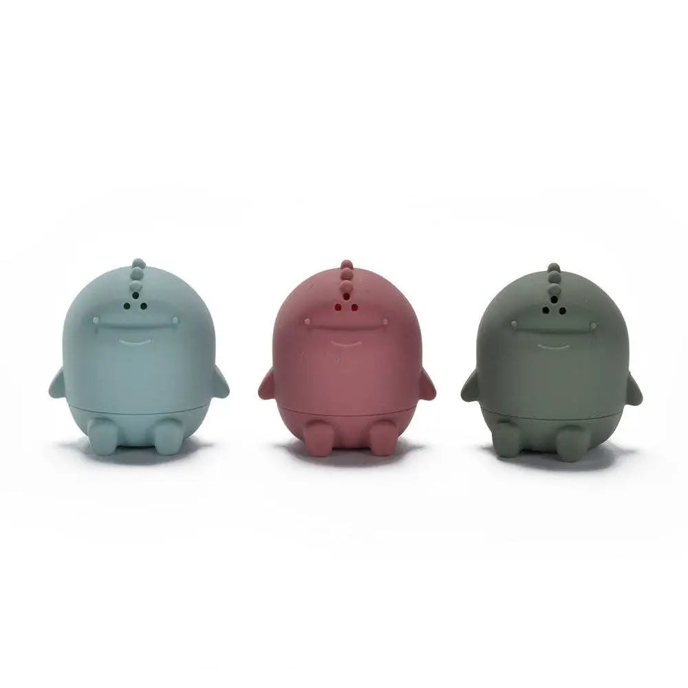 Three small rounded dinosaur-shaped figurines in pastel blue, dusty rose, and dark grey, arranged side by side on a white background.