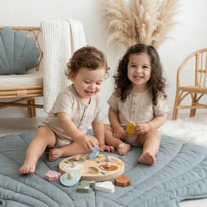 Two children playing with wooden toys on a quilted blanket in a cozy room.