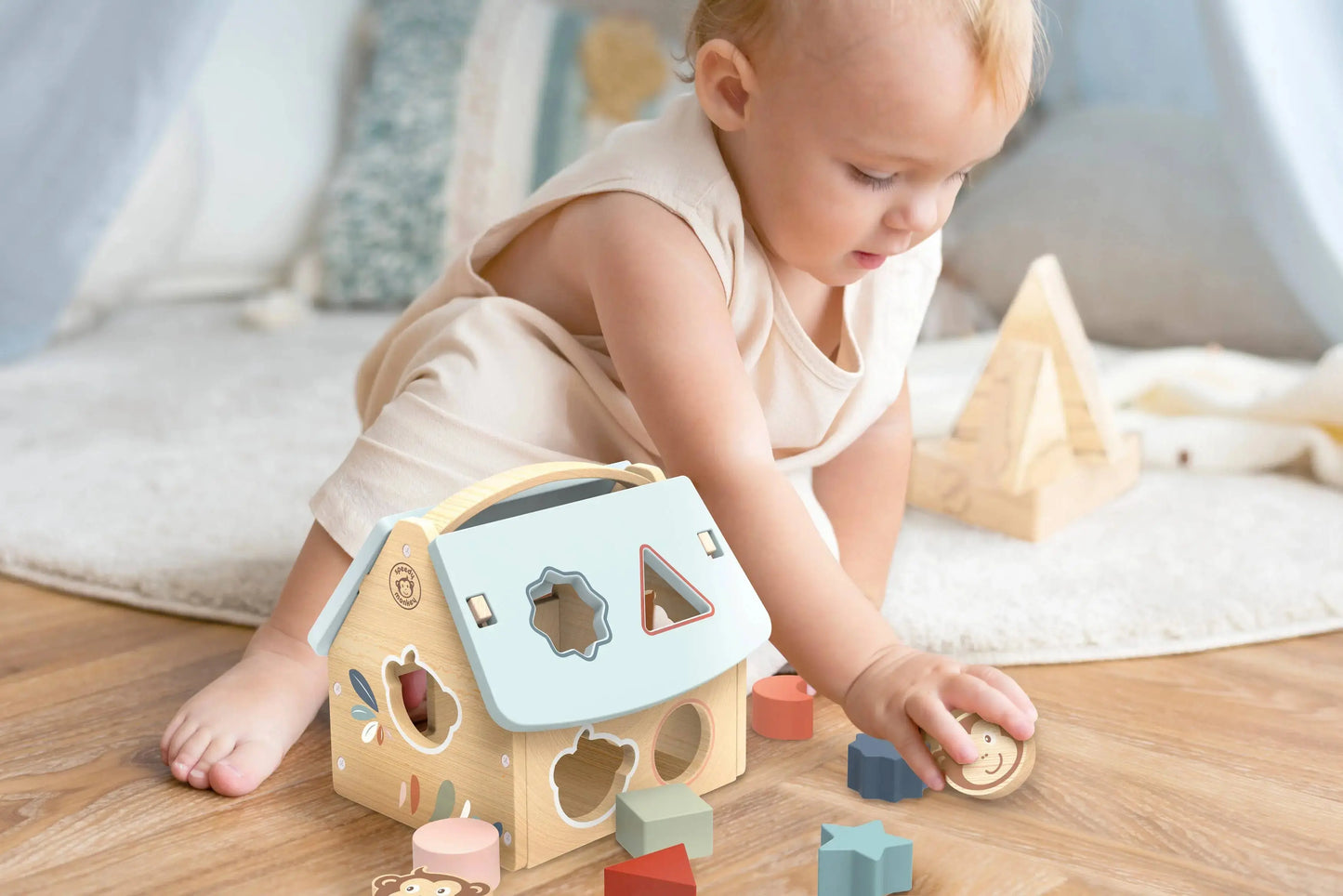 Baby playing with a shape sorter toy on a wooden floor.