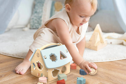 Baby playing with a shape sorter toy on a wooden floor.