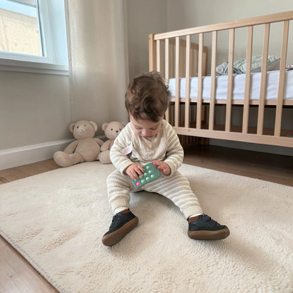 Child playing with a toy phone on a rug in a nursery
