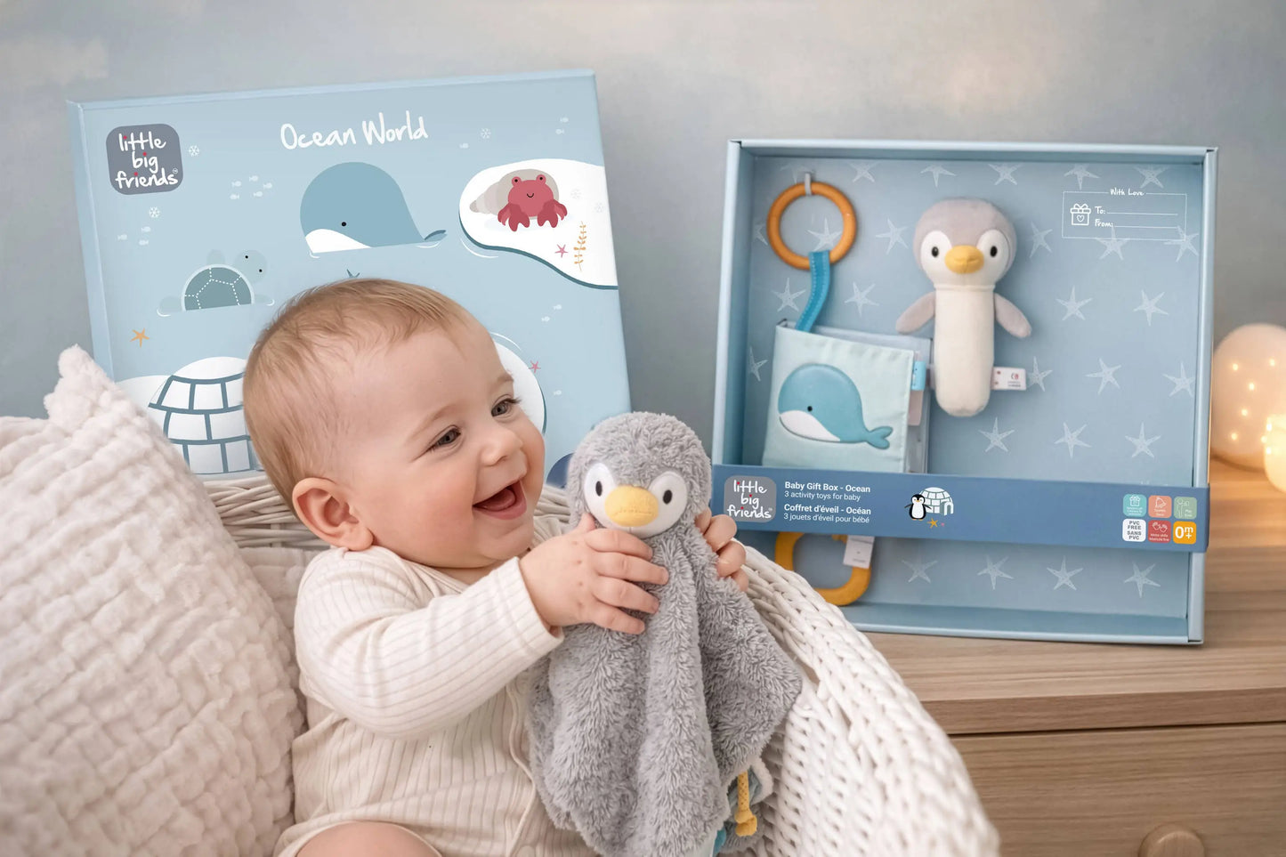 Baby holding a plush toy with 'Little Big Friends' packaging in the background