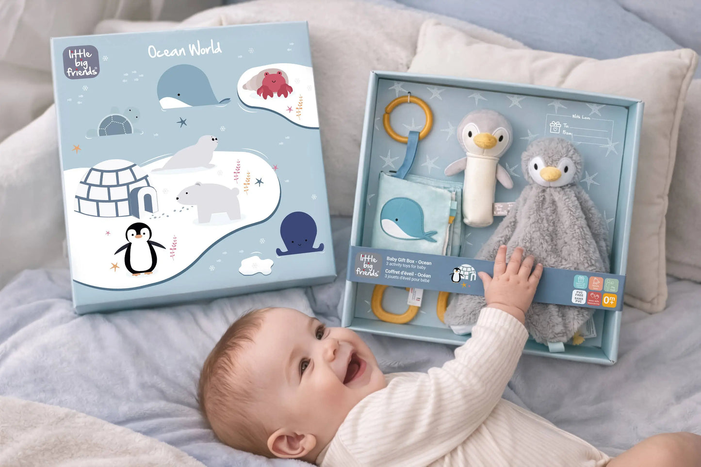 Baby interacting with a toy set in a box labelled 'Little Big Friends' on a bed.