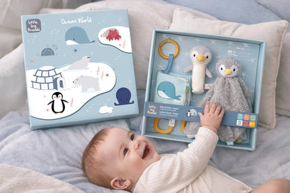 Baby interacting with a toy set in a box labelled 'Little Big Friends' on a bed.