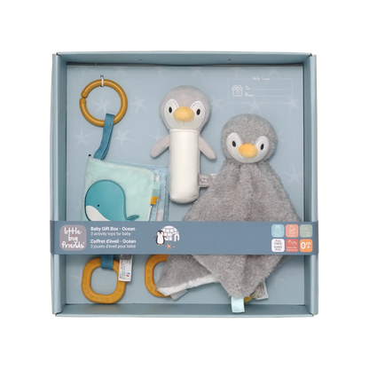 A baby gift set by Little Big Friends inside a light blue box, featuring a plush penguin toy, a grey penguin comforter, a blue whale fabric toy, and wooden ring toys.
