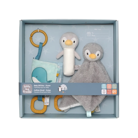 A baby gift set by Little Big Friends inside a light blue box, featuring a plush penguin toy, a grey penguin comforter, a blue whale fabric toy, and wooden ring toys.