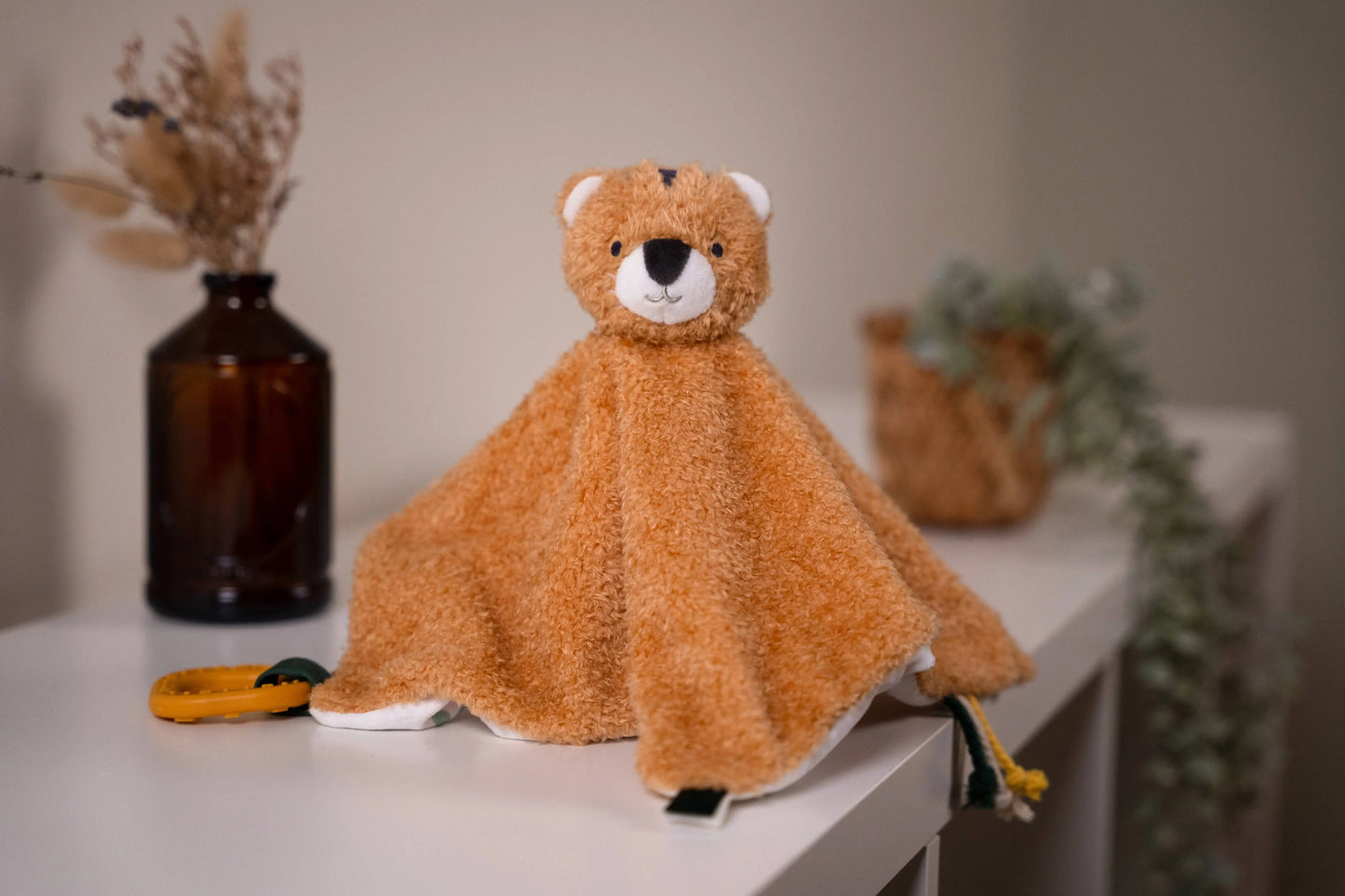 Brown teddy bear-shaped comfort blanket on a white surface with decorative elements in the background.
