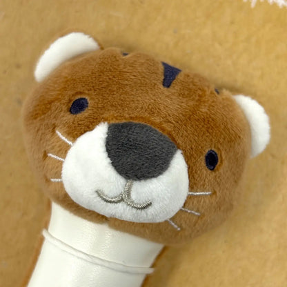 A close-up of a brown plush toy head shaped like a tiger face, with white inner ears, white muzzle, dark grey nose, and small dark eyes, attached to a white handle against a tan background.