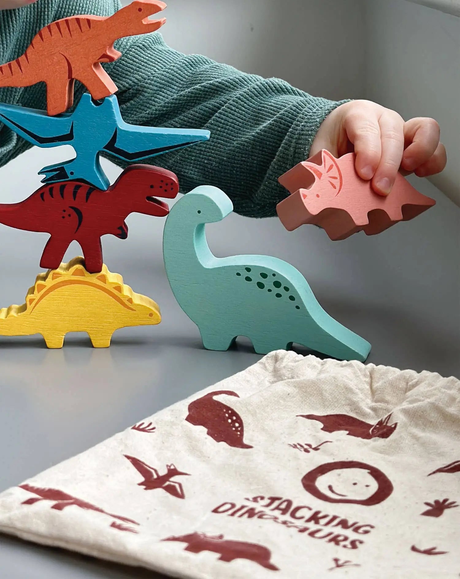 Child playing with colourful wooden dinosaur toys on a light surface.
