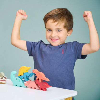 Child with arms raised next to colourful dinosaur toys on a table