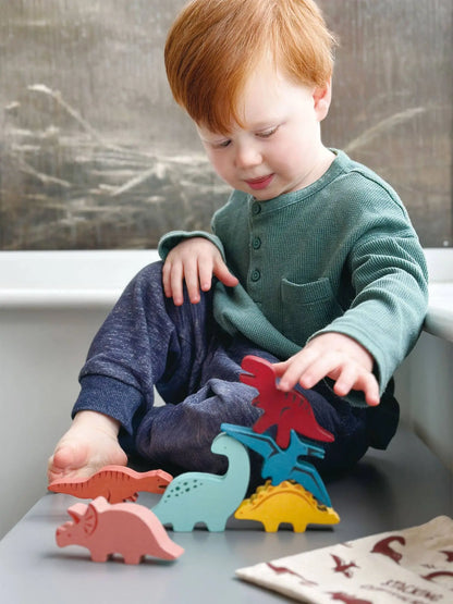 Child playing with colourful wooden dinosaur toys on a table.