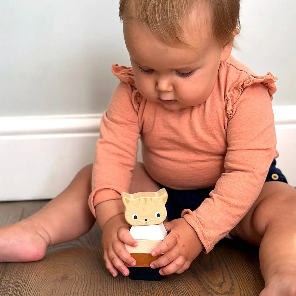 Baby holding a toy with a cat design on a wooden floor.