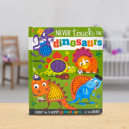 A children's hardcover board book titled 'Never touch the dinosaurs' standing upright on a light wooden surface with a softly blurred indoor background.
