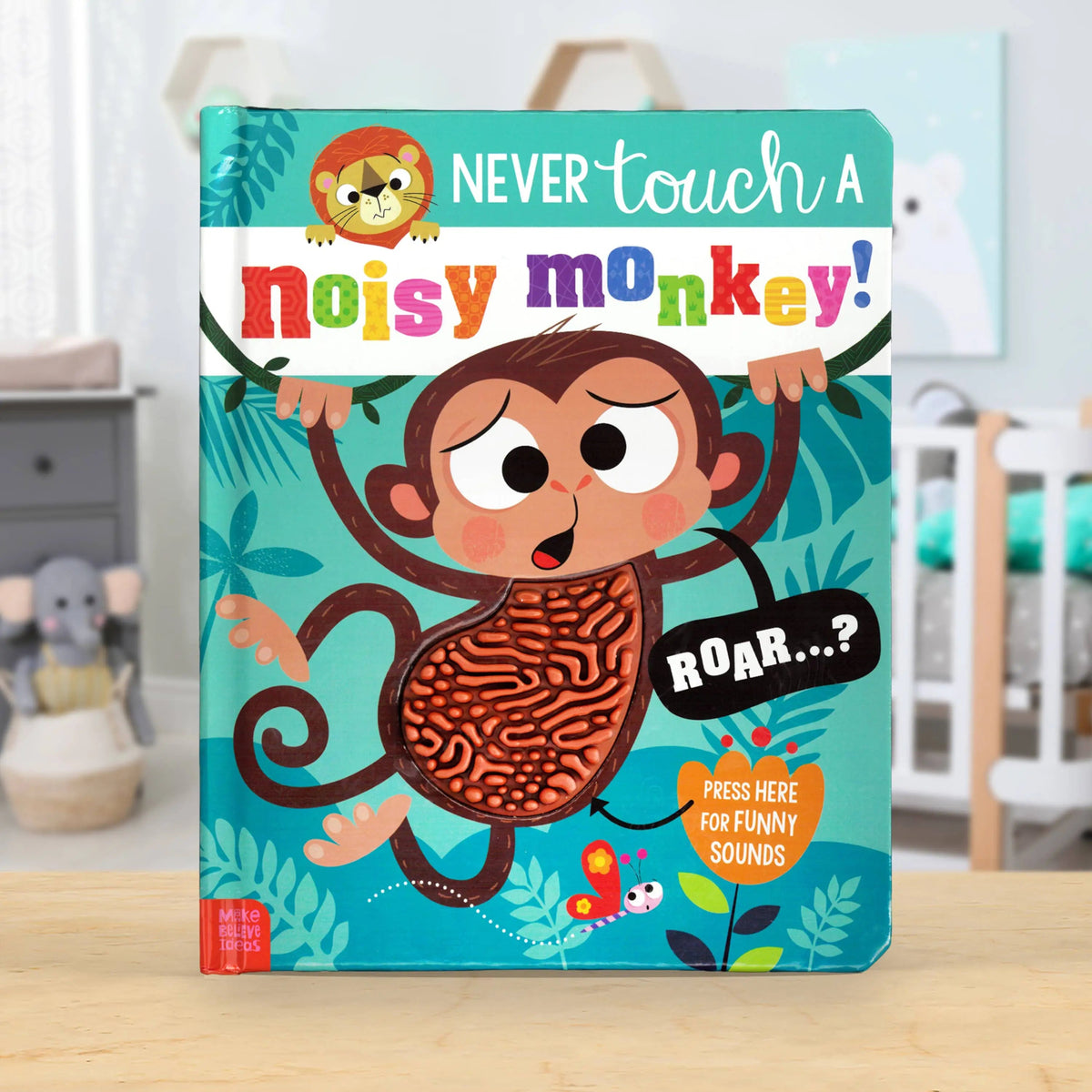 A children's board book titled 'Never touch a noisy monkey!' standing upright on a wooden surface in a nursery setting. The cover features a cartoon monkey with a textured, sound-making body and colourful playful text.