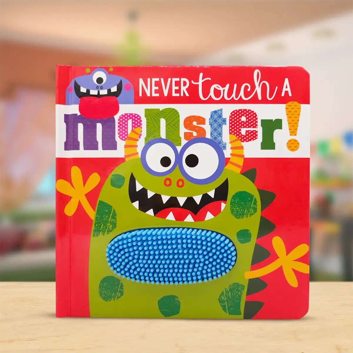 Children's book titled 'Never Touch a Monster' with colourful monster illustration on a wooden surface.