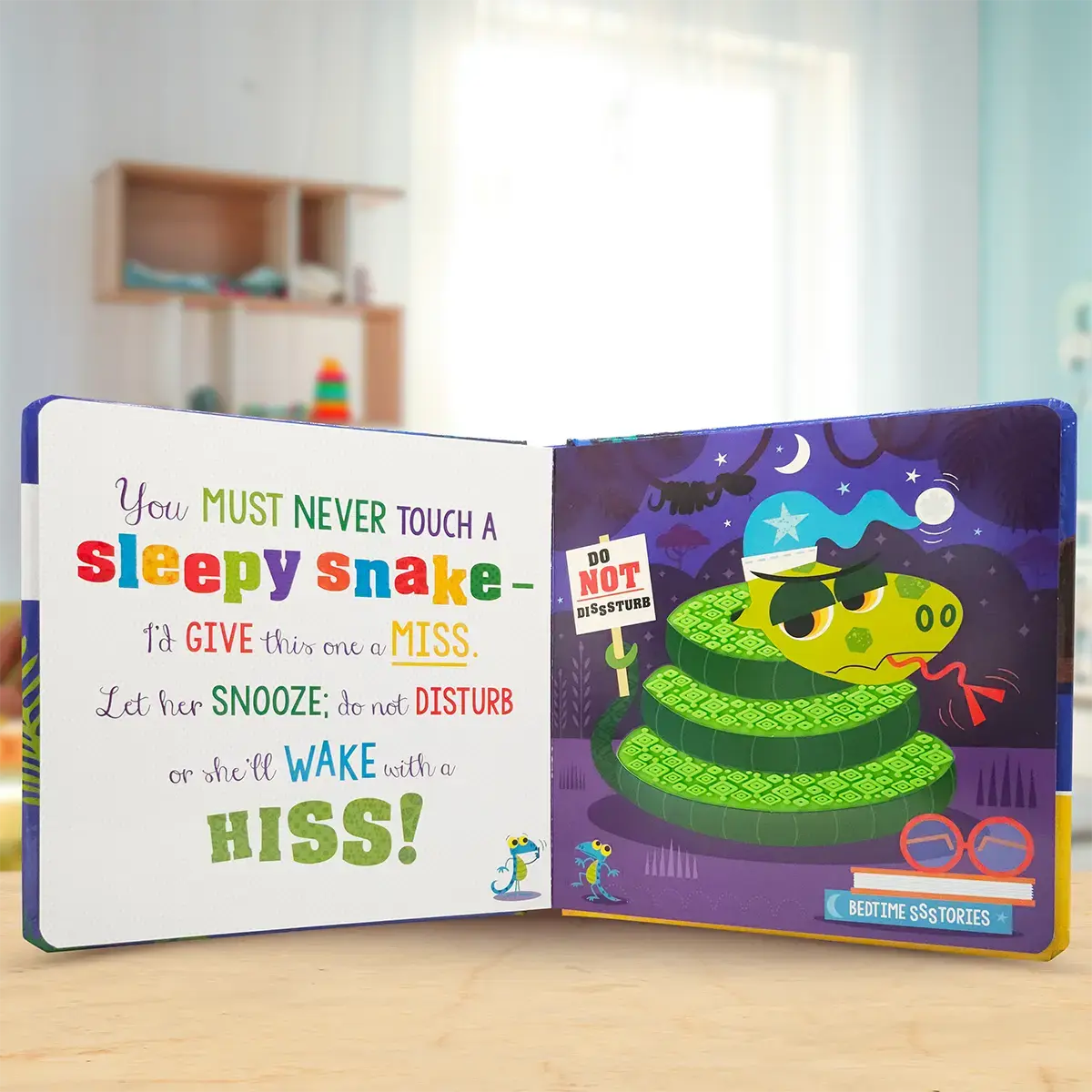 Children's book open to a page with a green snake illustration and text on a wooden surface.