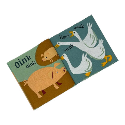 A children's wooden sound book with colourful illustrations of farm animals, including pigs, geese, and ducks, with printed words like 'Oink', 'Oink', 'Honk', and 'Quack'.