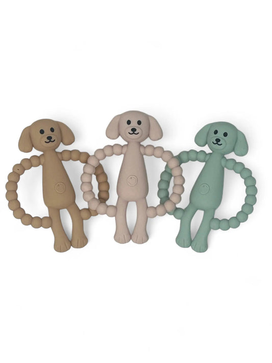 Three dog-shaped teething rings in pink, beige, and blue on a white background