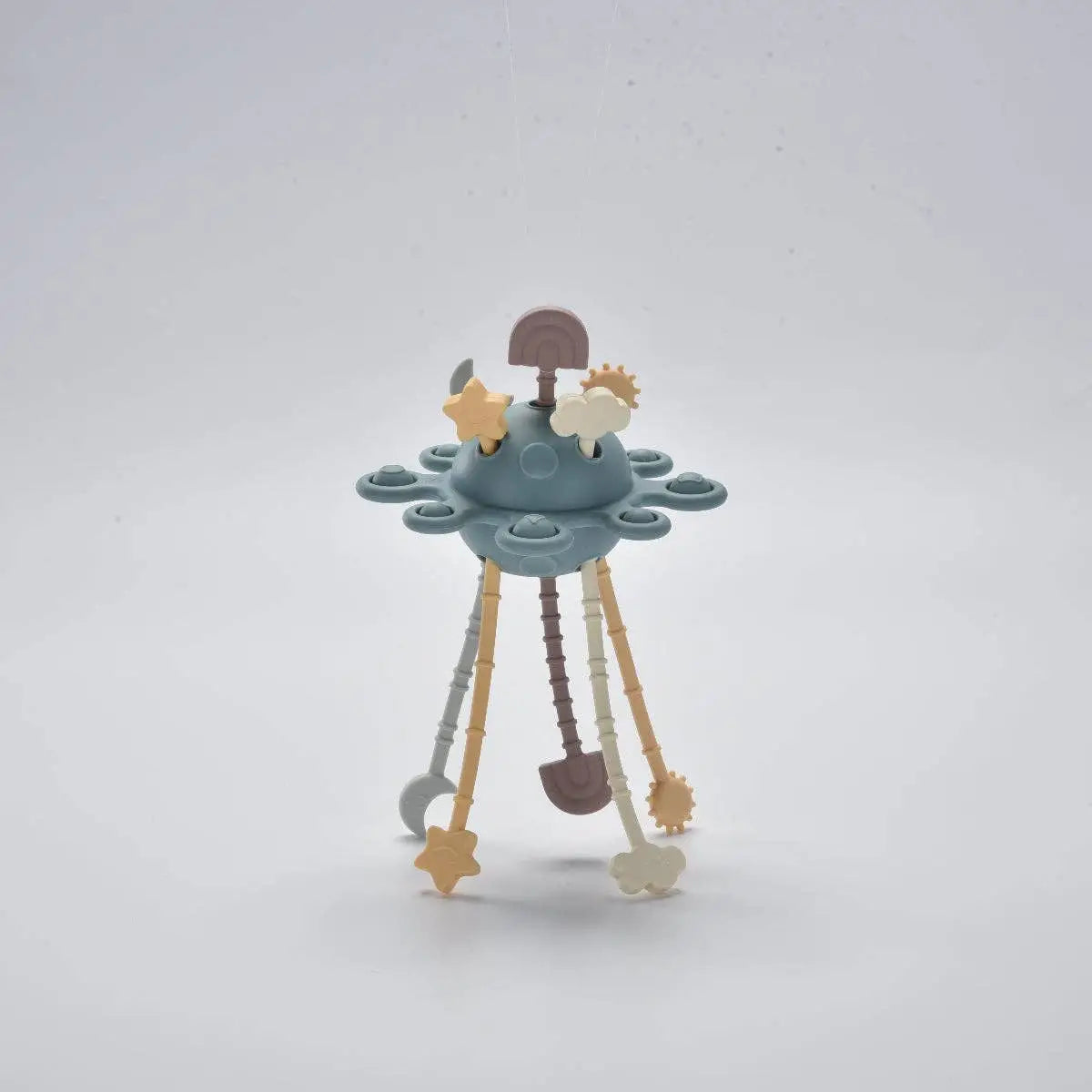 A pastel-coloured baby activity toy shaped like a small space station or UFO, featuring a blue-grey central dome, three hanging legs in beige, brown, and grey, and small star and gear accents.