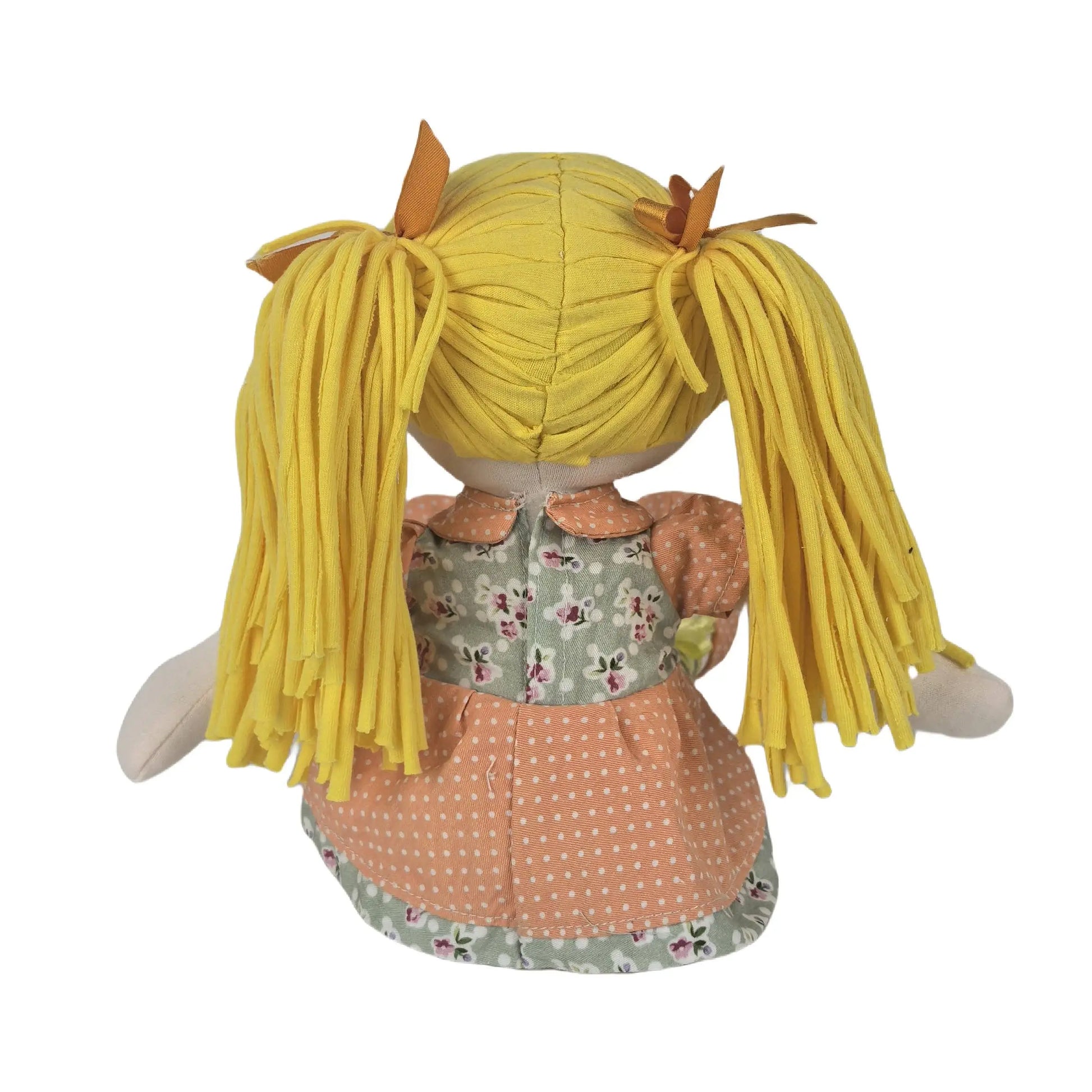 Back view of a plush doll with long yellow yarn-like pigtails, wearing a peach polka-dot skirt, a floral green bodice, and peach sleeves, shown on a white background.