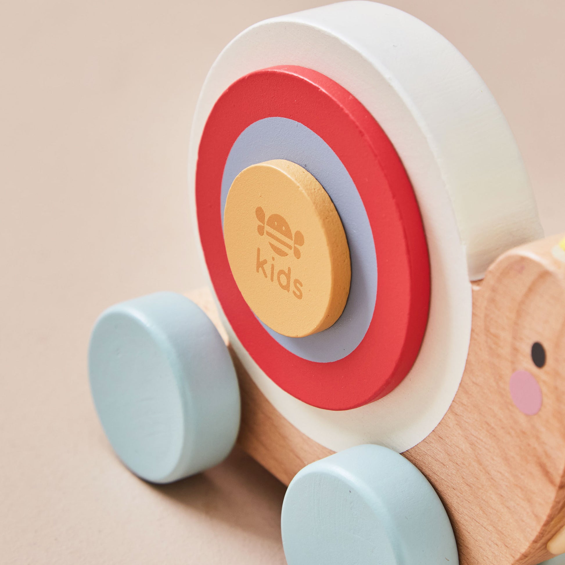 Wooden snail toy with colourful shell and a 'kids' button on a beige background