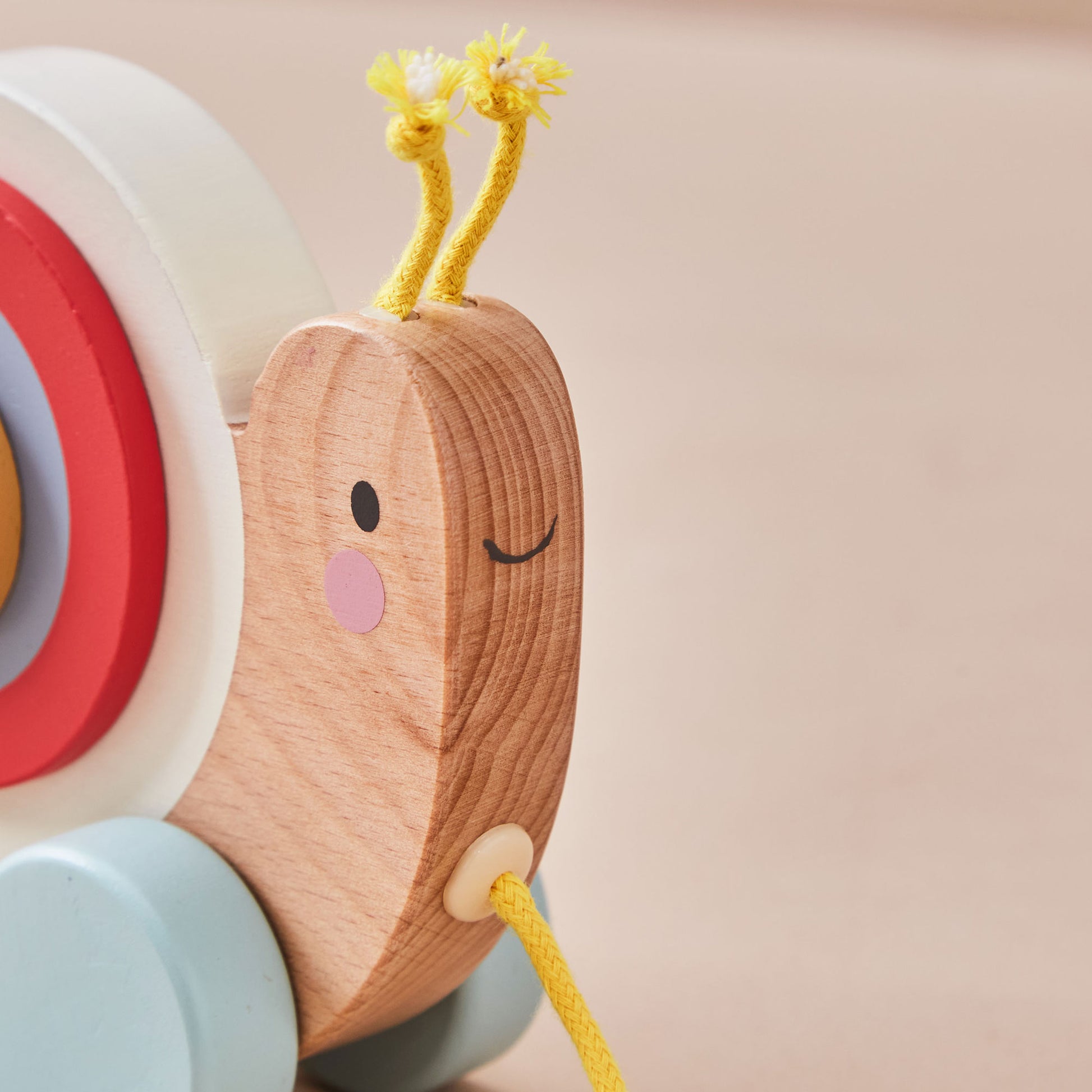 Wooden snail toy with a smiling face and colourful shell on a beige background