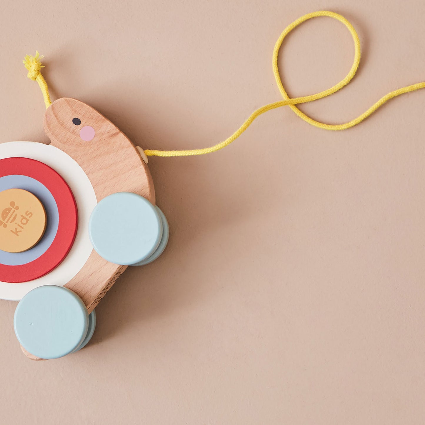 Wooden snail toy with colourful shell and a yellow string on a beige background