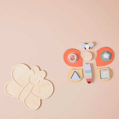 Dragonfly-shaped wooden toy with colourful elements on a beige background