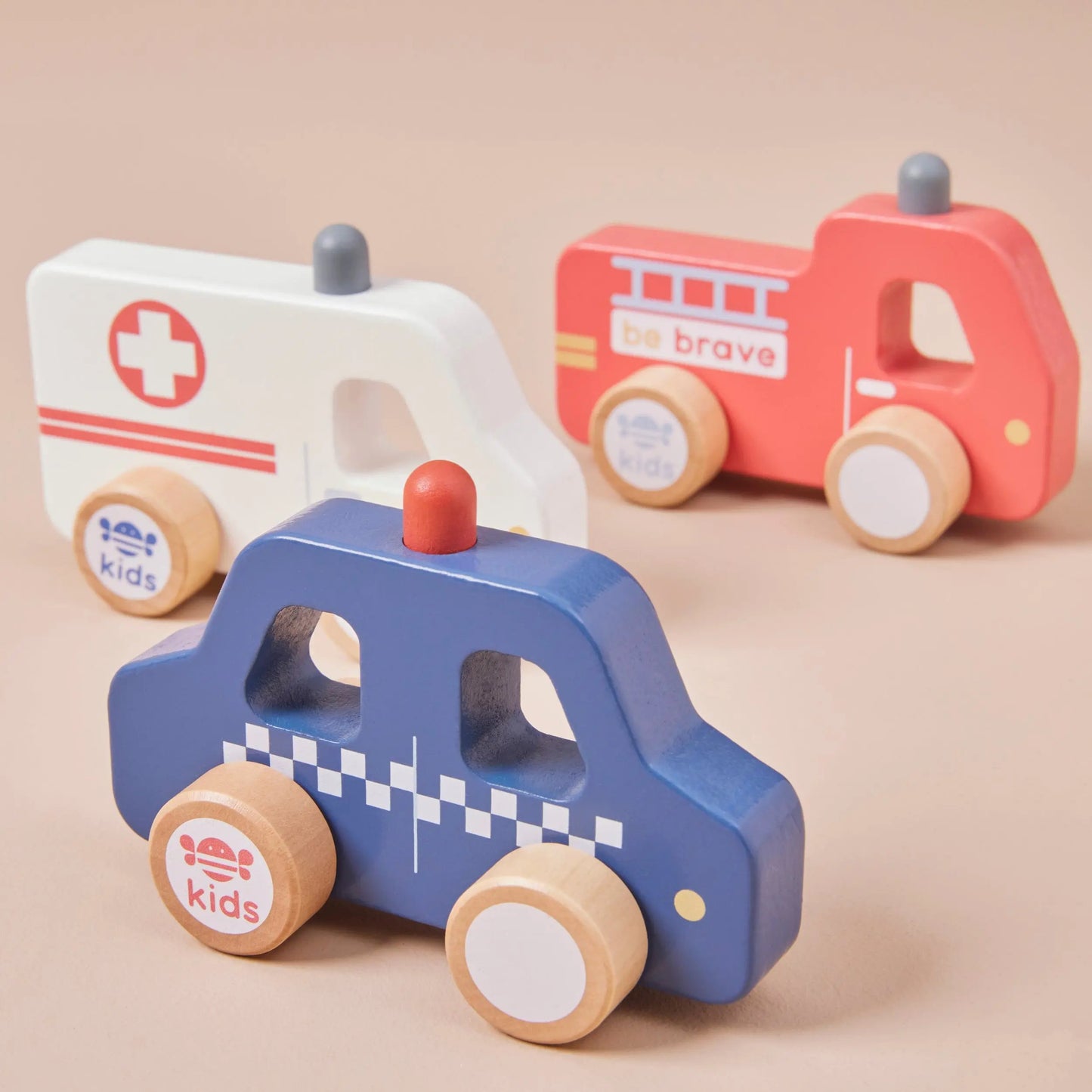 Set of wooden toy cars including an ambulance, fire truck, and police car on a beige background.